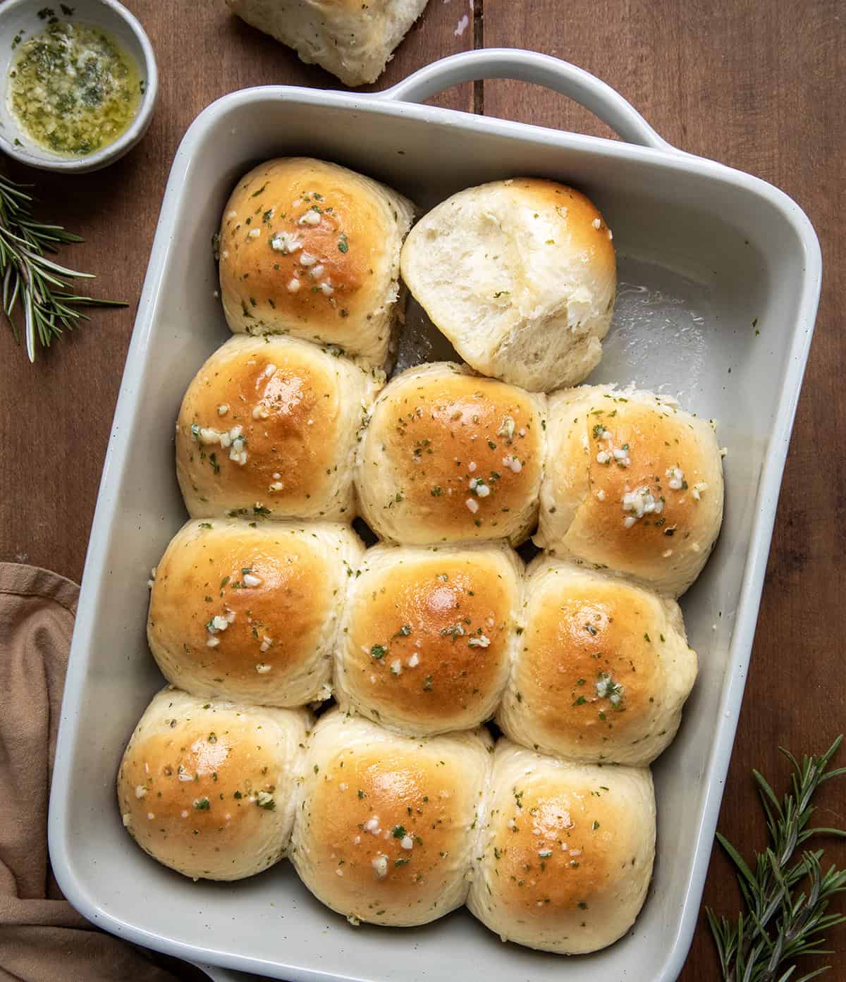 Pan of Rosemary Dinner Rolls on a wooden table with one roll removed and one on its side.