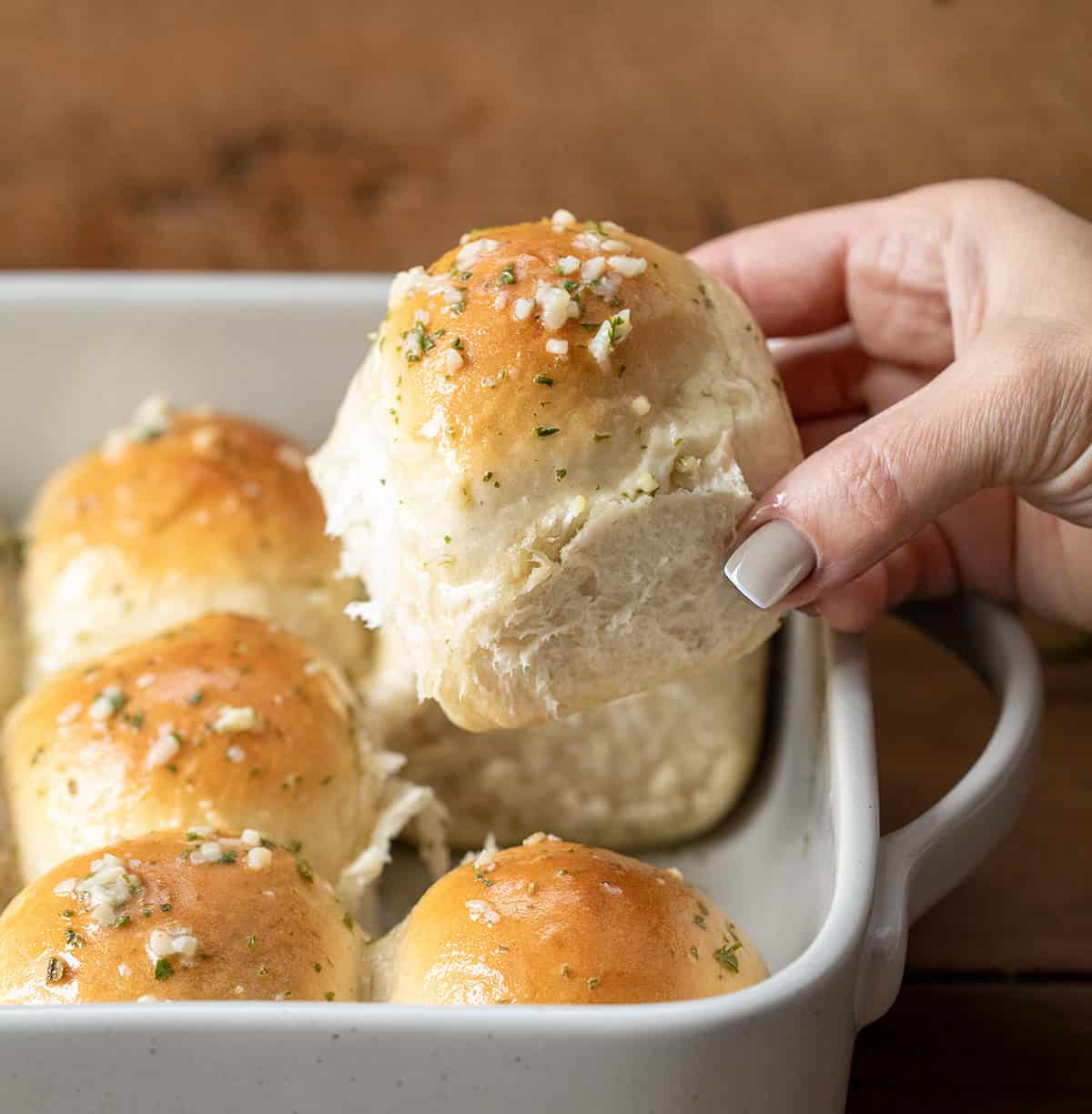 Hand picking up a Rosemary Dinner Roll from the pan.