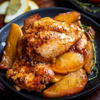 Close up of a Apple Chicken Thigh on a bed of apples on a wooden table.