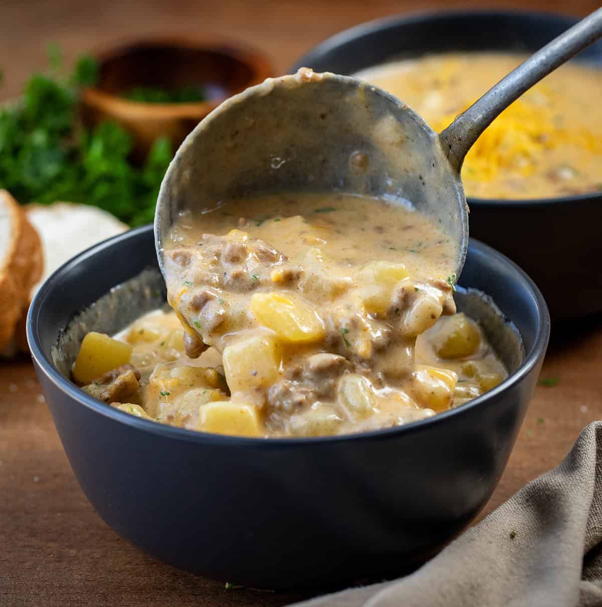 Ladleing Cheesy Beef and Potato Soup into a black bowl.