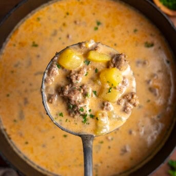 Ladle holding a full amount of Cheesy Beef and Potato Soup over the pot.