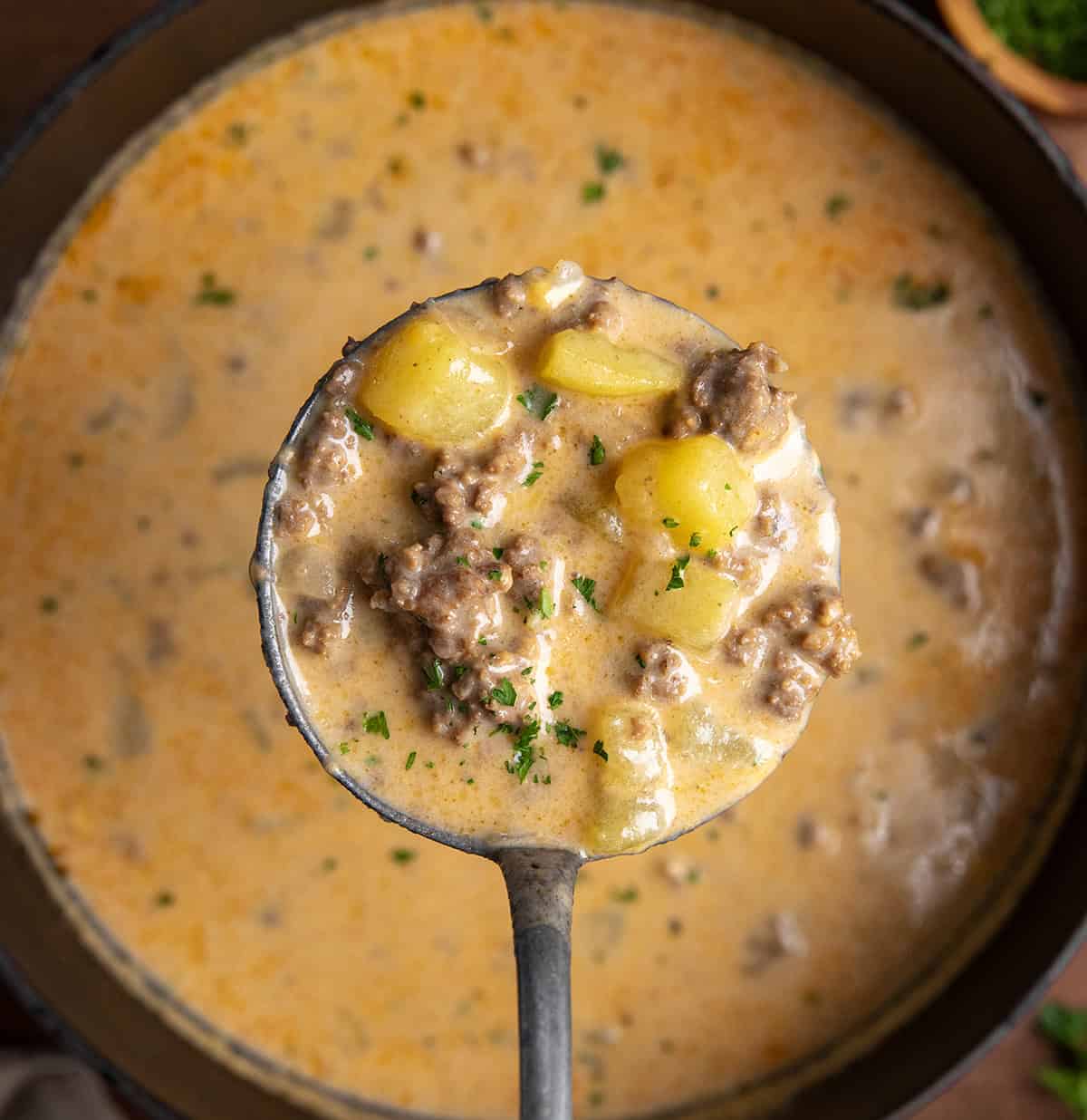 Ladle holding a full amount of Cheesy Beef and Potato Soup over the pot. 