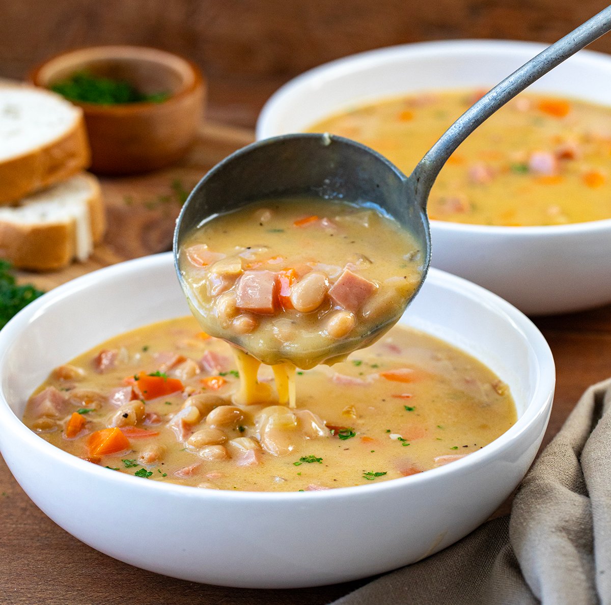 Using a ladle to add Cheesy Ham and Bean Soup to a bowl.