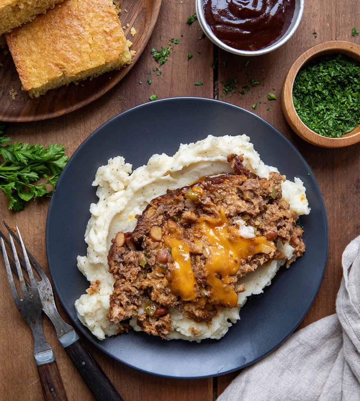 Slice of Cowboy Meatloaf on mashed potatoes on a wooden table from overhead.