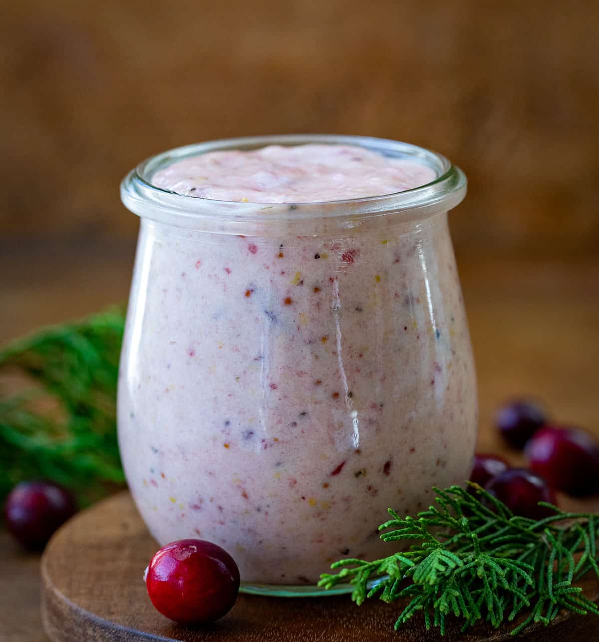 Jar of Cranberry Aioli on a wooden table with fresh cranberries. 