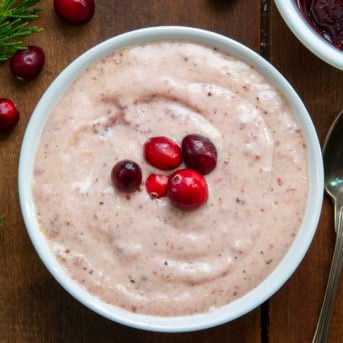 Bowl of Cranberry Aioli with fresh cranberries on top on a wooden table from overhead.