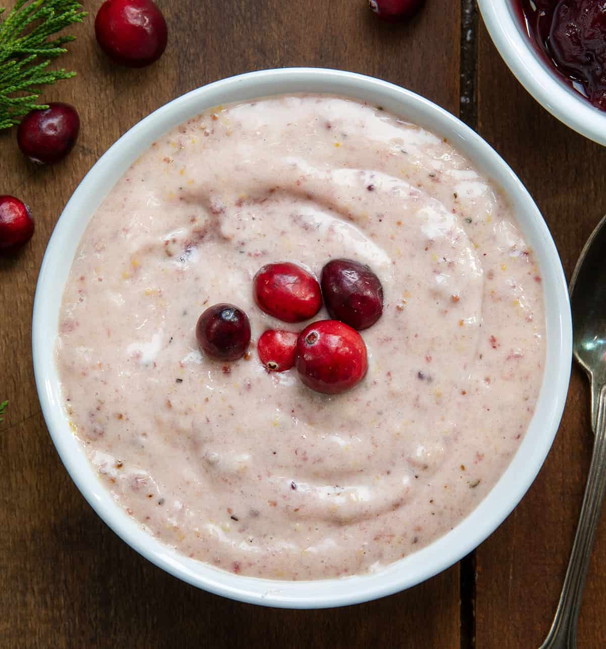 Bowl of Cranberry Aioli with fresh cranberries on top on a wooden table from overhead.