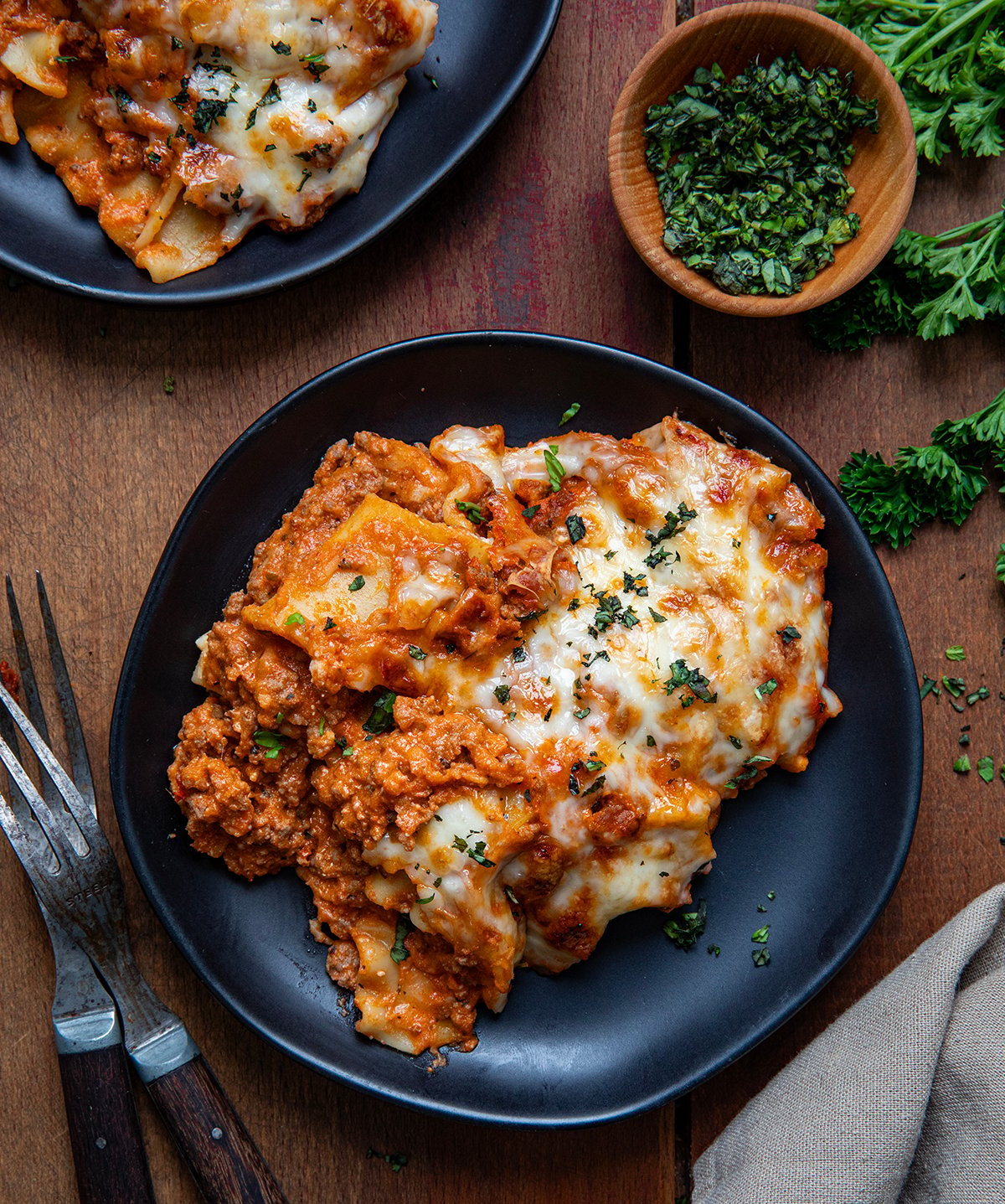 Black plates with Easy Lasagna Casserole on them on a wooden table from overhead.