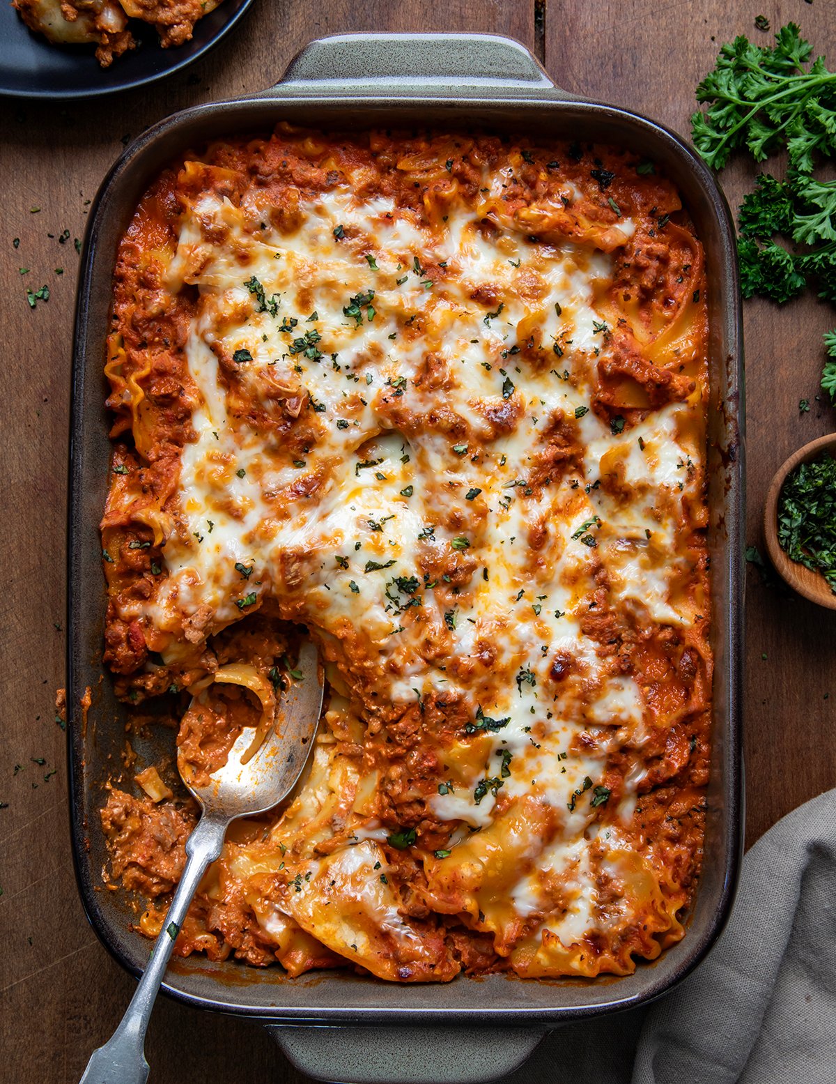 Pan of Easy Lasagna Casserole with a portion removed and a spoon in the pan on a wooden table from overhead.