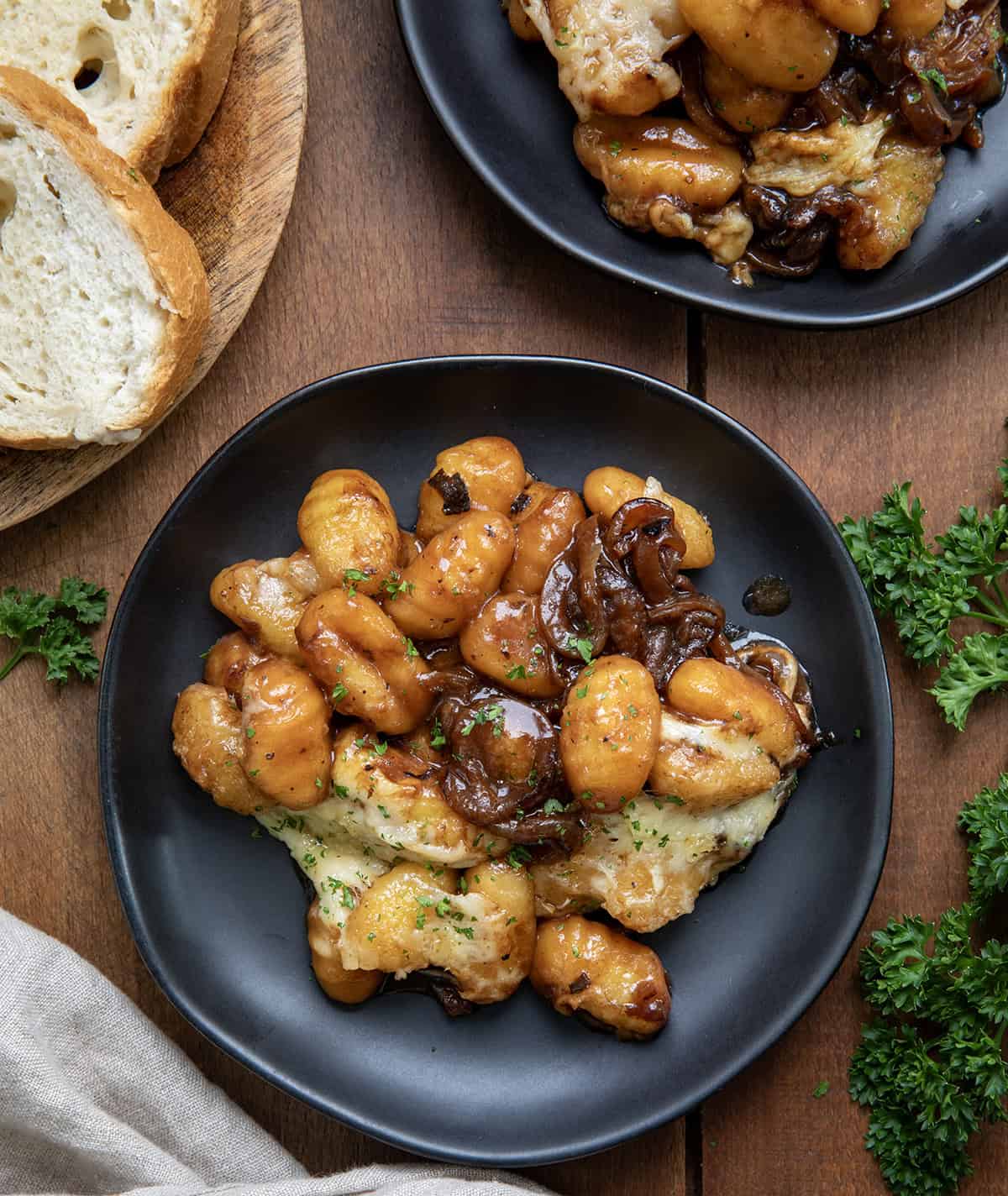 Black plates with French Onion Gnocchi on them on a wooden table shot from overhead.