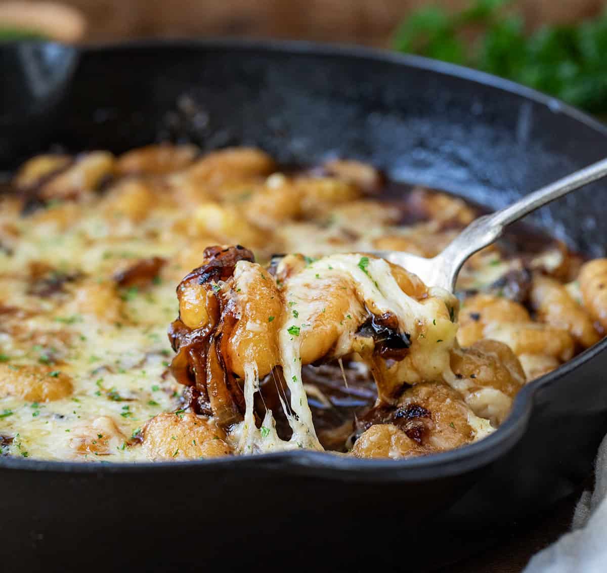 Scooping up a spoonful of French Onion Gnocchi from skillet.