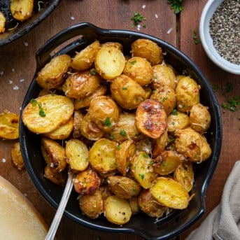 Bowl of Garlic Parmesan Roasted Potatoes on a wooden table with a spoon from overhead.