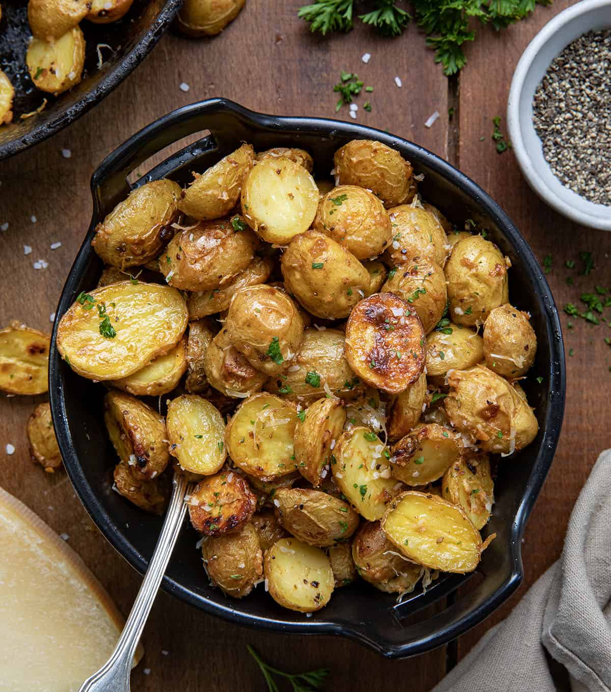 Bowl of Garlic Parmesan Roasted Potatoes on a wooden table with a spoon from overhead.