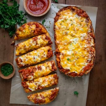 Lasagna Garlic Bread on a wooden table with one cut into slices.