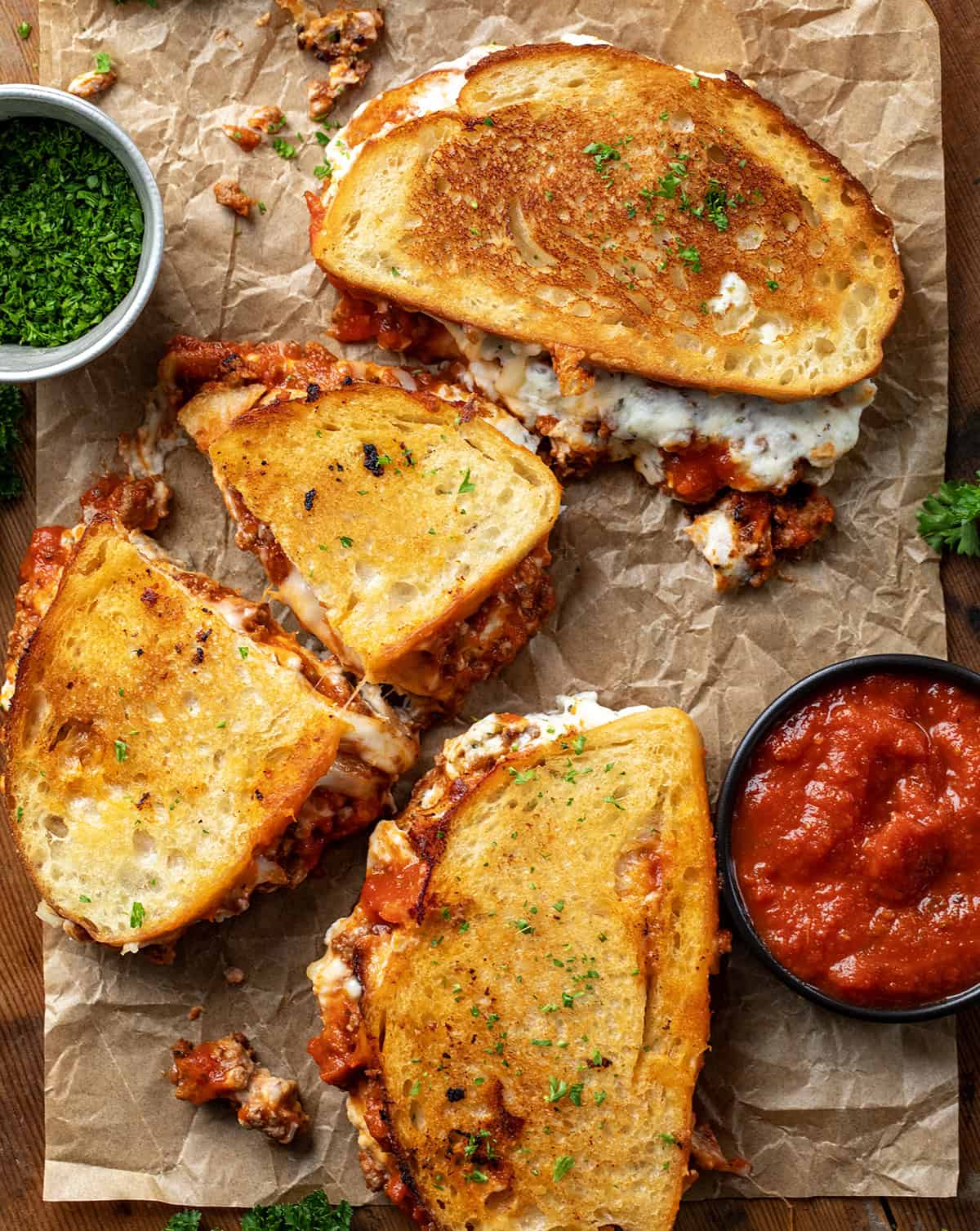 Lasagna Grilled Cheese sandwiches on a piece of parchment paper with marinara sauce from overhead. 