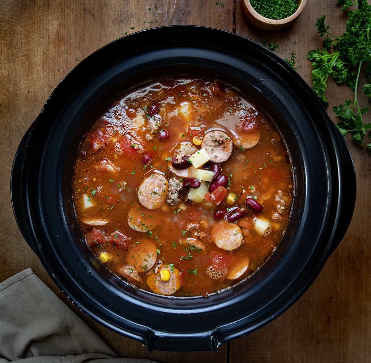 Slow Cooker Cowboy Soup in a crock pot on a wooden table from overhead. 