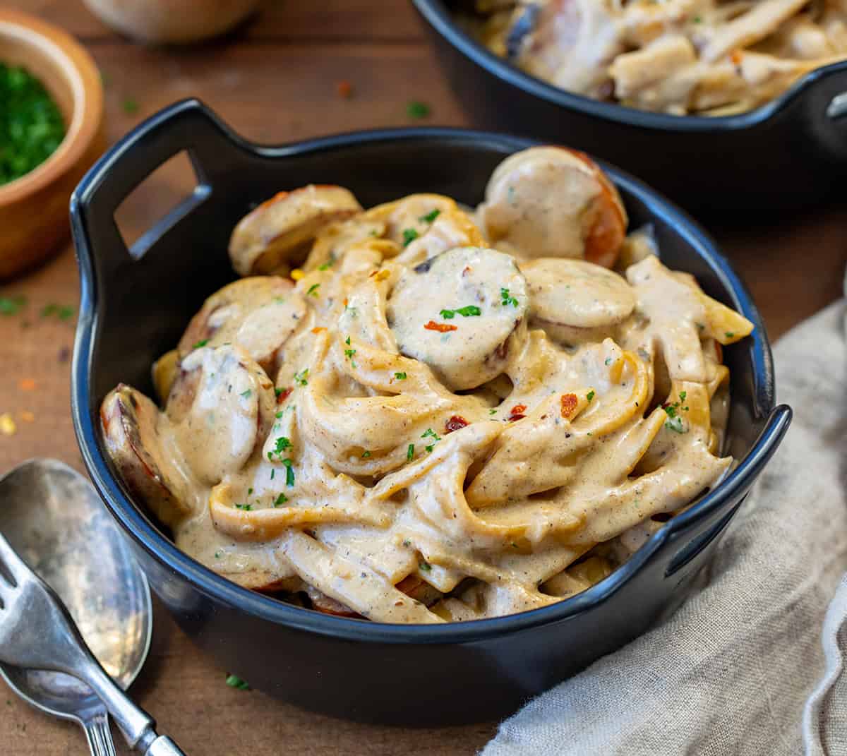 Mini Skillet bowls of Smoked Sausage Cajun Alfredo on a wooden table.