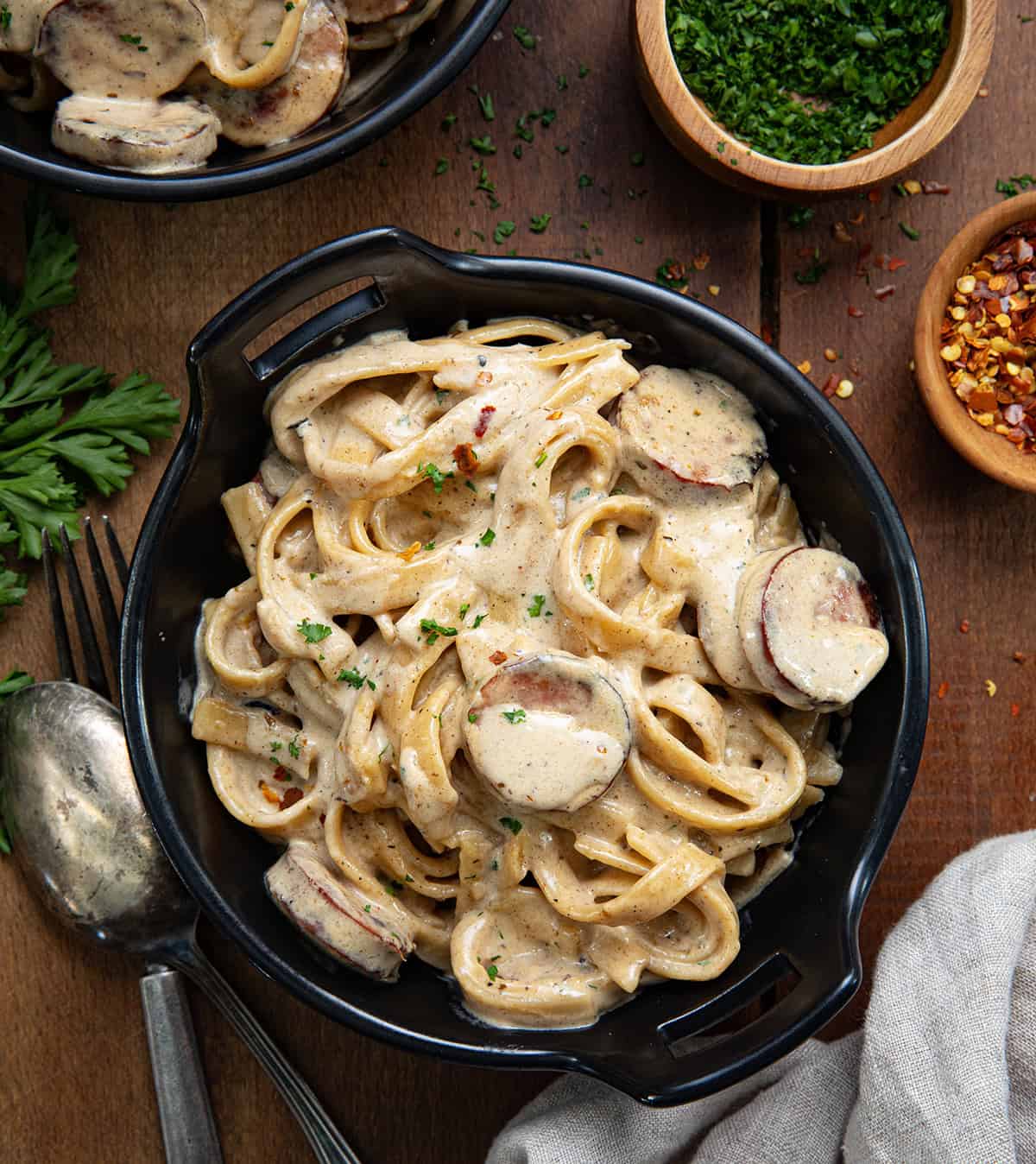 Mini Skillet bowls of Smoked Sausage Cajun Alfredo on a wooden table from overhead.