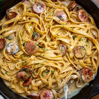 CLose up of creamy Smoked Sausage Cajun Alfredo in skillet with spoon resting in the sauce.