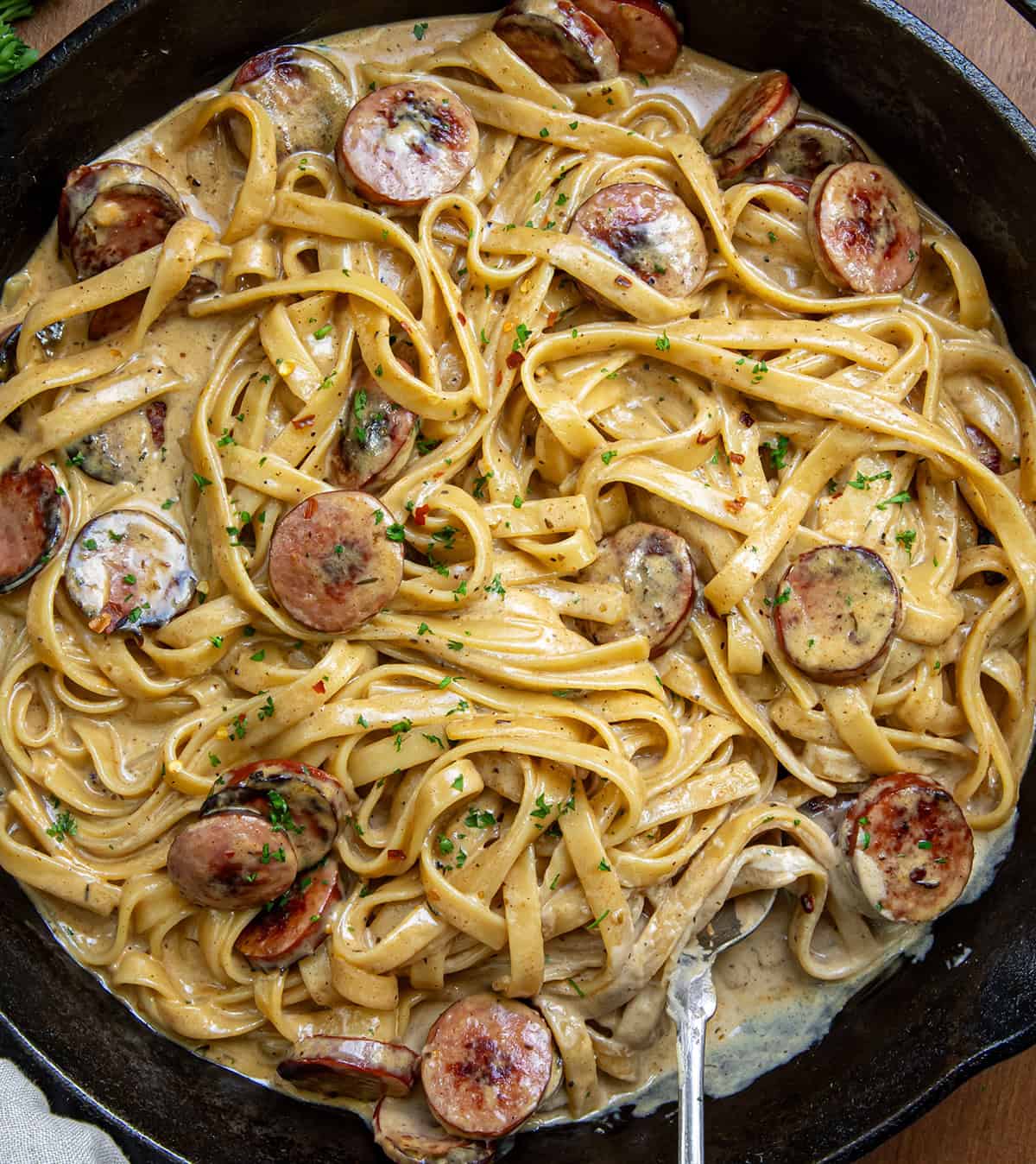 CLose up of creamy Smoked Sausage Cajun Alfredo in skillet with spoon resting in the sauce.