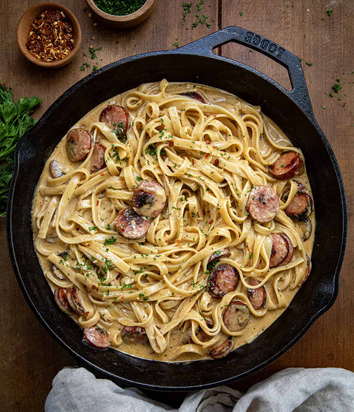 Skillet of Smoked Sausage Cajun Alfredo on a wooden table with towel from overhead. 