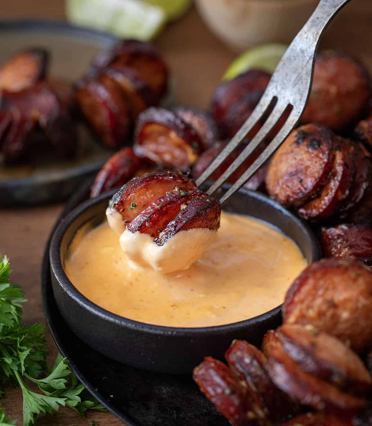 Dipping Spicy Sriracha Hasselback Kielbasa Bites into sauce.