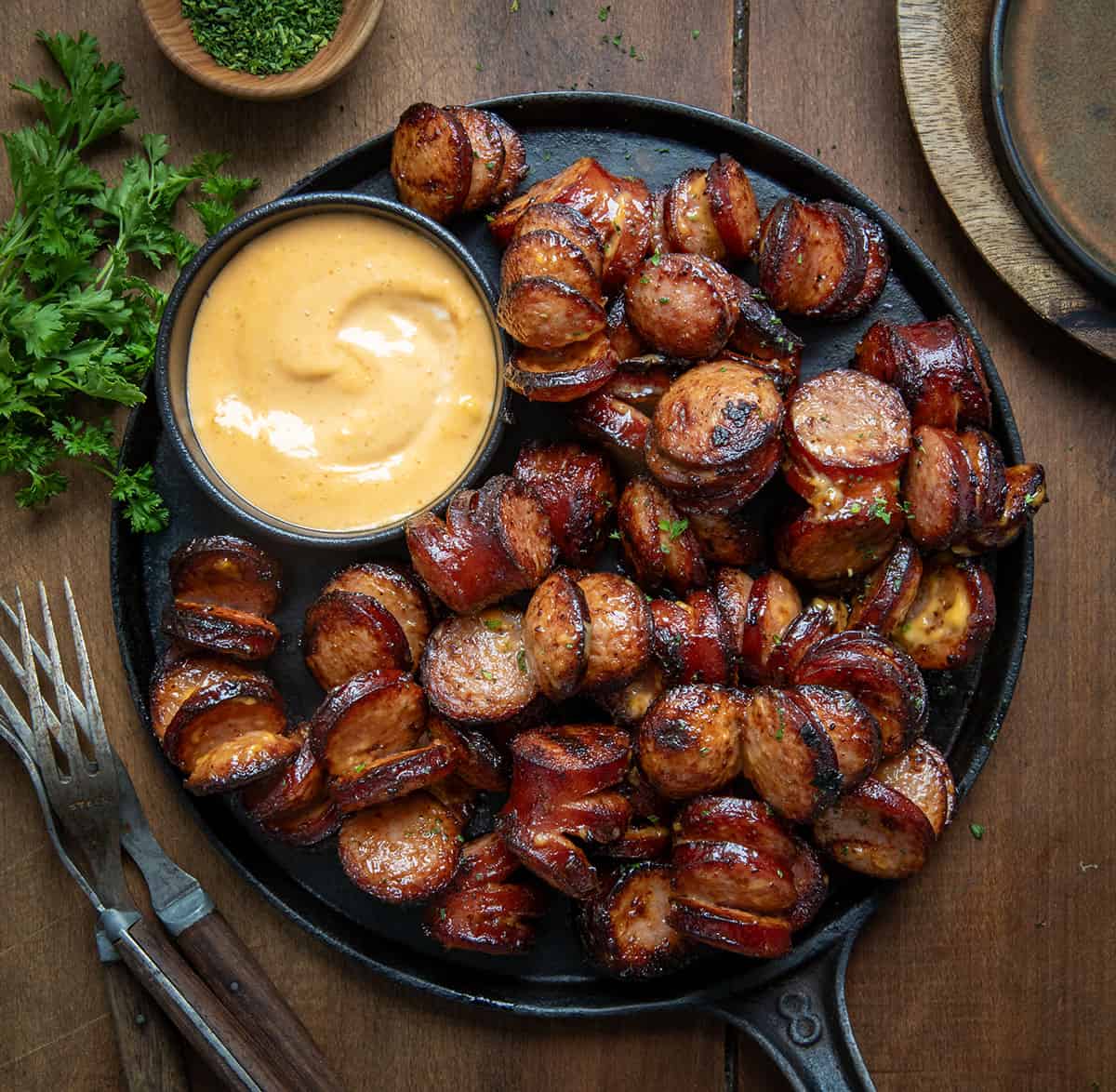 Skillet of Spicy Sriracha Hasselback Kielbasa Bites on a wooden table from overhead.