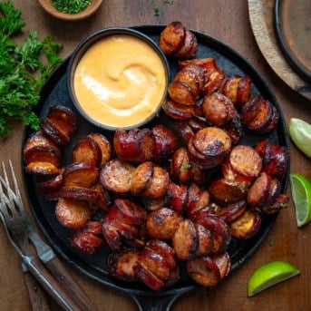 Skillet of Spicy Sriracha Hasselback Kielbasa Bites on a wooden table from overhead.