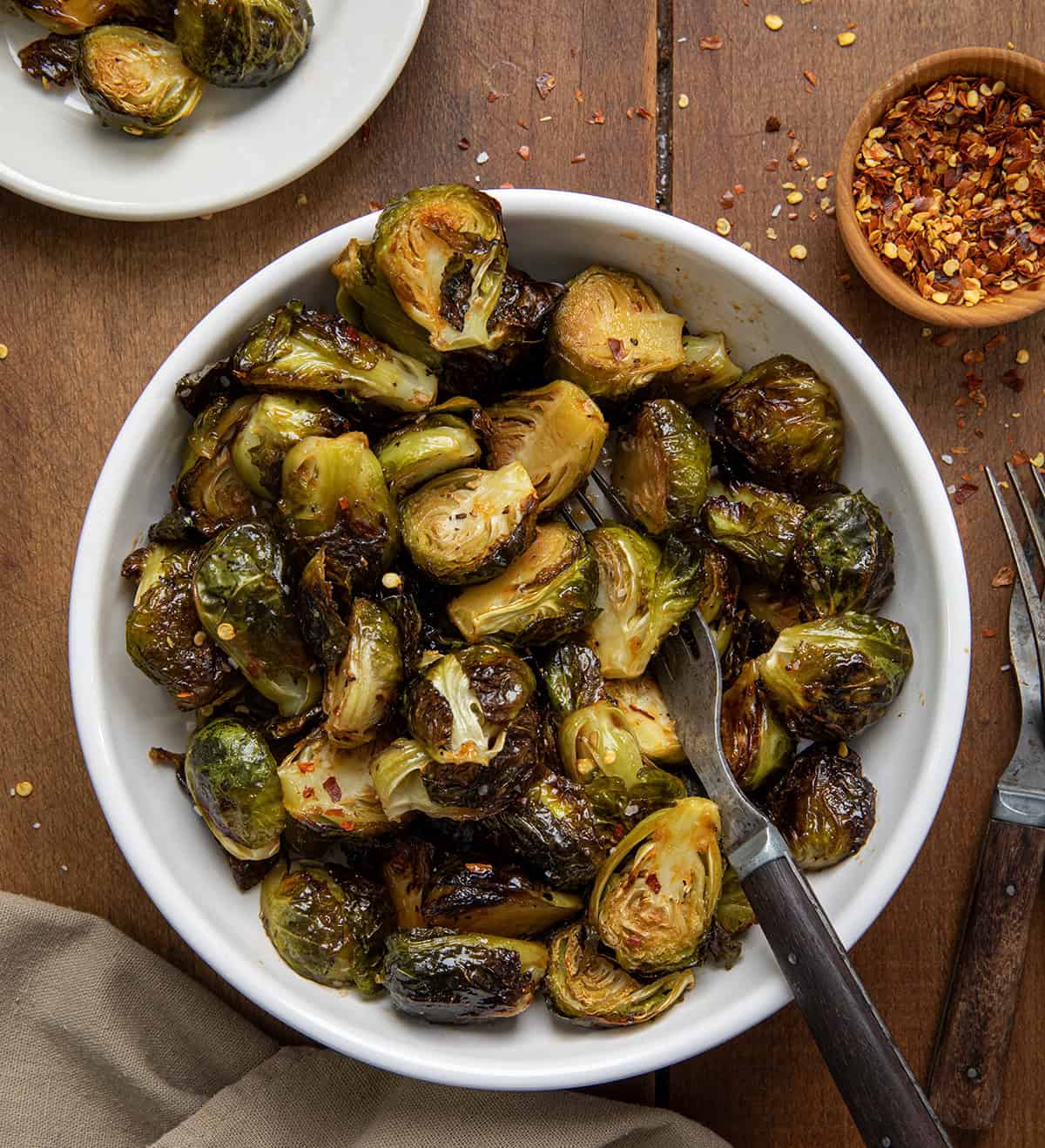 Bowl of Sweet Sriracha Brussels Sprouts with a fork in it on a wooden table from overhead.