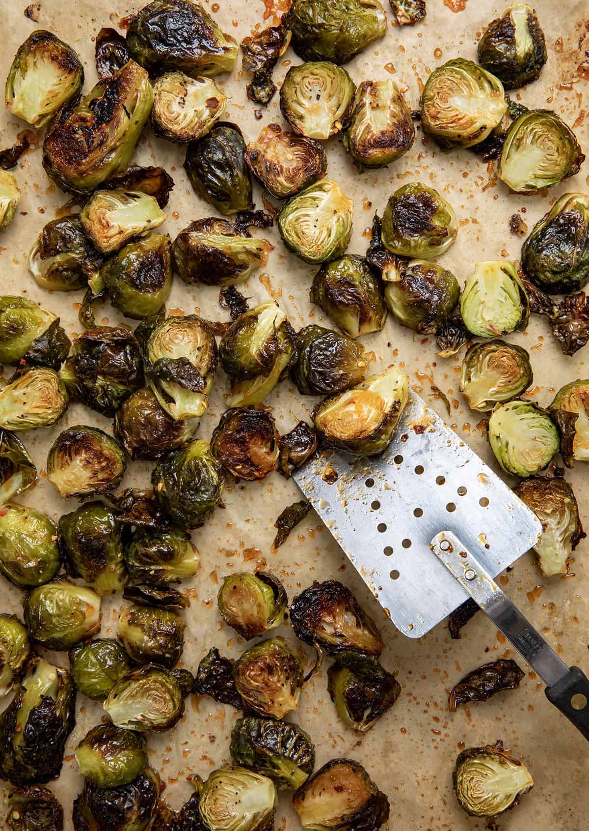 Sweet Sriracha Brussels Sprouts on a baking sheet lined with parchment paper and a spatula on the side.