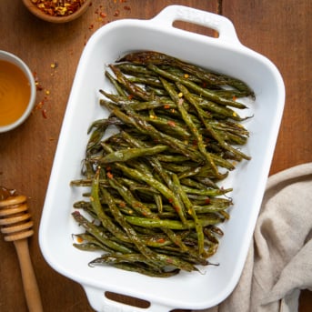 Tray of Sweet and Spicy Green Beans on a wooden table with honey and hot pepper flakes.