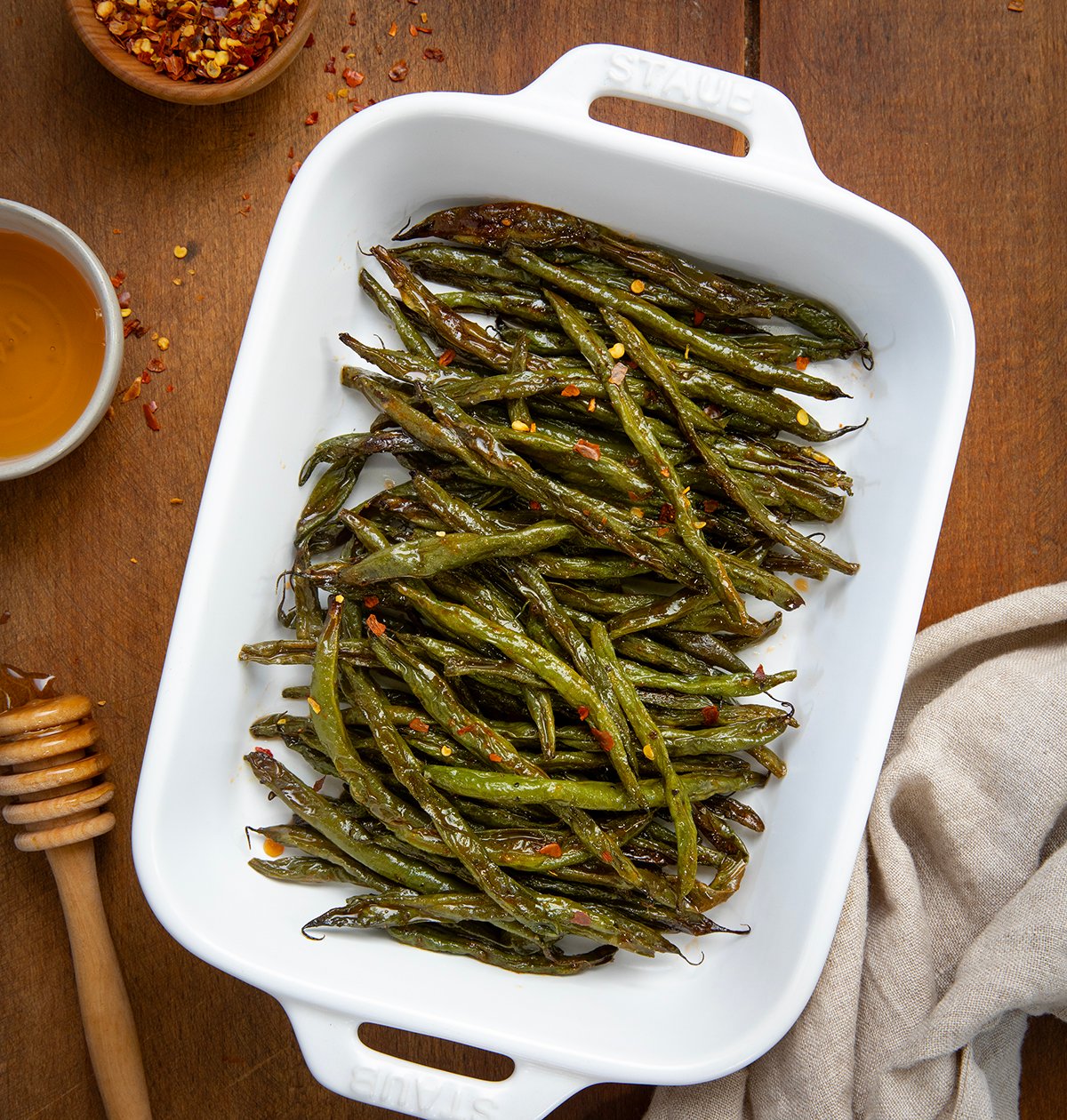 Tray of Sweet and Spicy Green Beans on a wooden table with honey and hot pepper flakes.