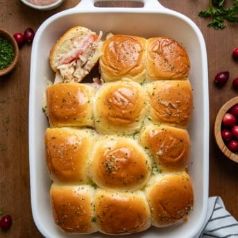 Pan of Turkey Melt Sliders with Cranberry Aioli with one slider on its side on a wooden table from overhead.