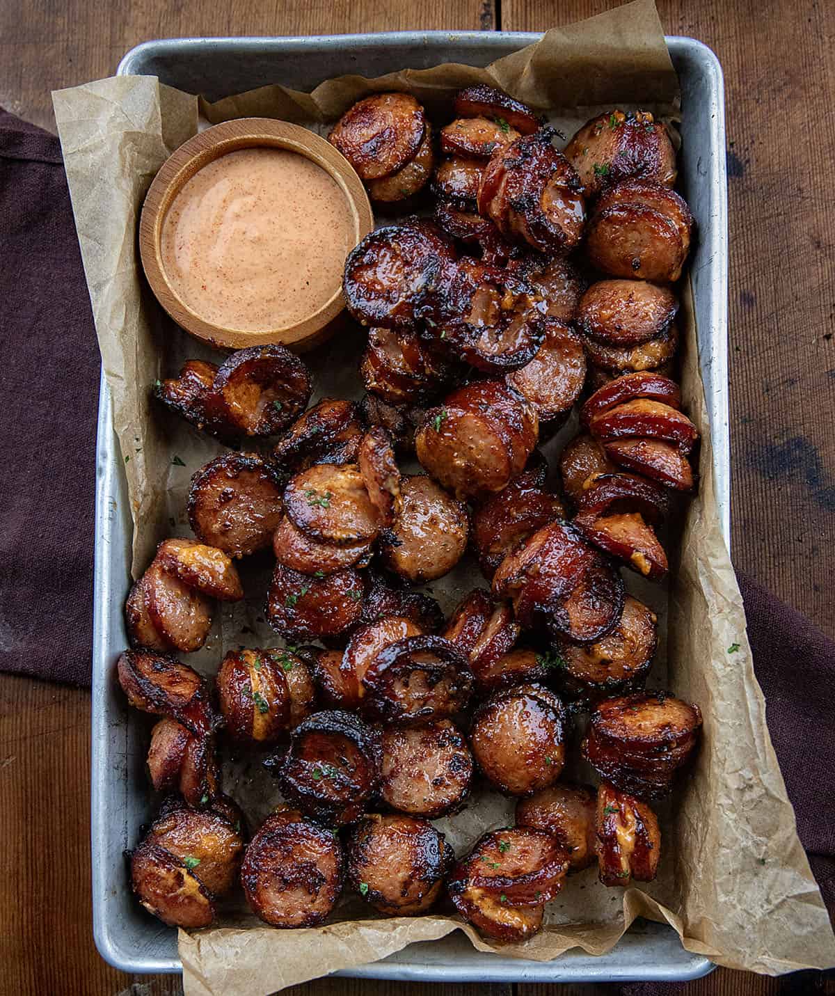 Pan of Chipotle Aioli Hasselback Kielbasa Bites on a wooden table from overhead.