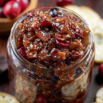 Jar of Cranberry Bacon Jam on a wooden table surrounded by bagel chips.