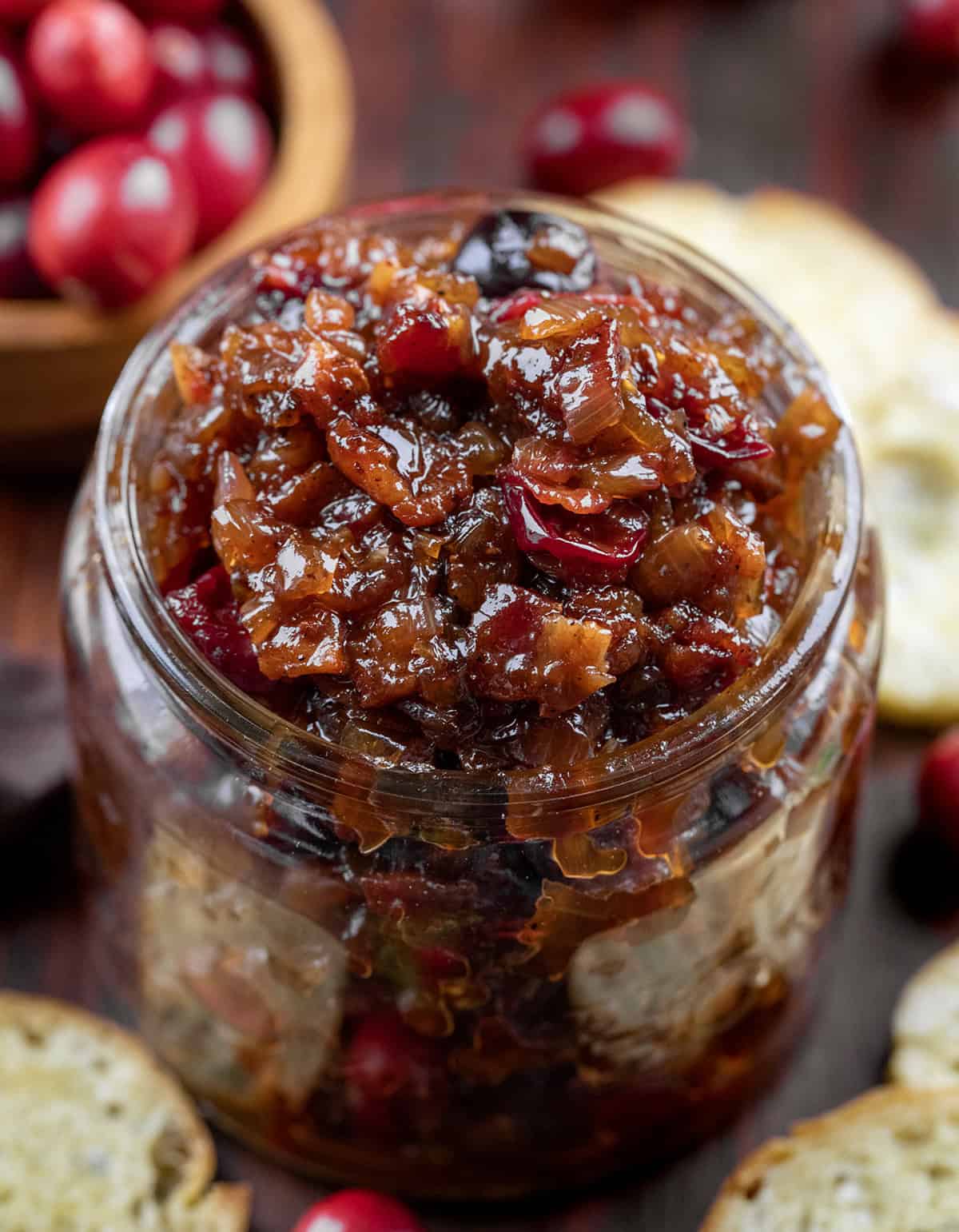 Jar of Cranberry Bacon Jam on a wooden table surrounded by bagel chips.