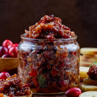 Jar of Cranberry Bacon Jam on a wooden table with fresh cranberries.