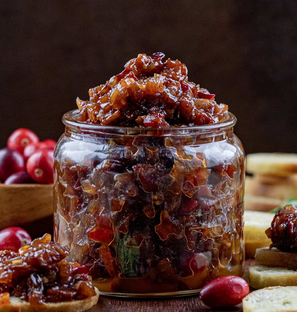 Jar of Cranberry Bacon Jam on a wooden table with fresh cranberries. 