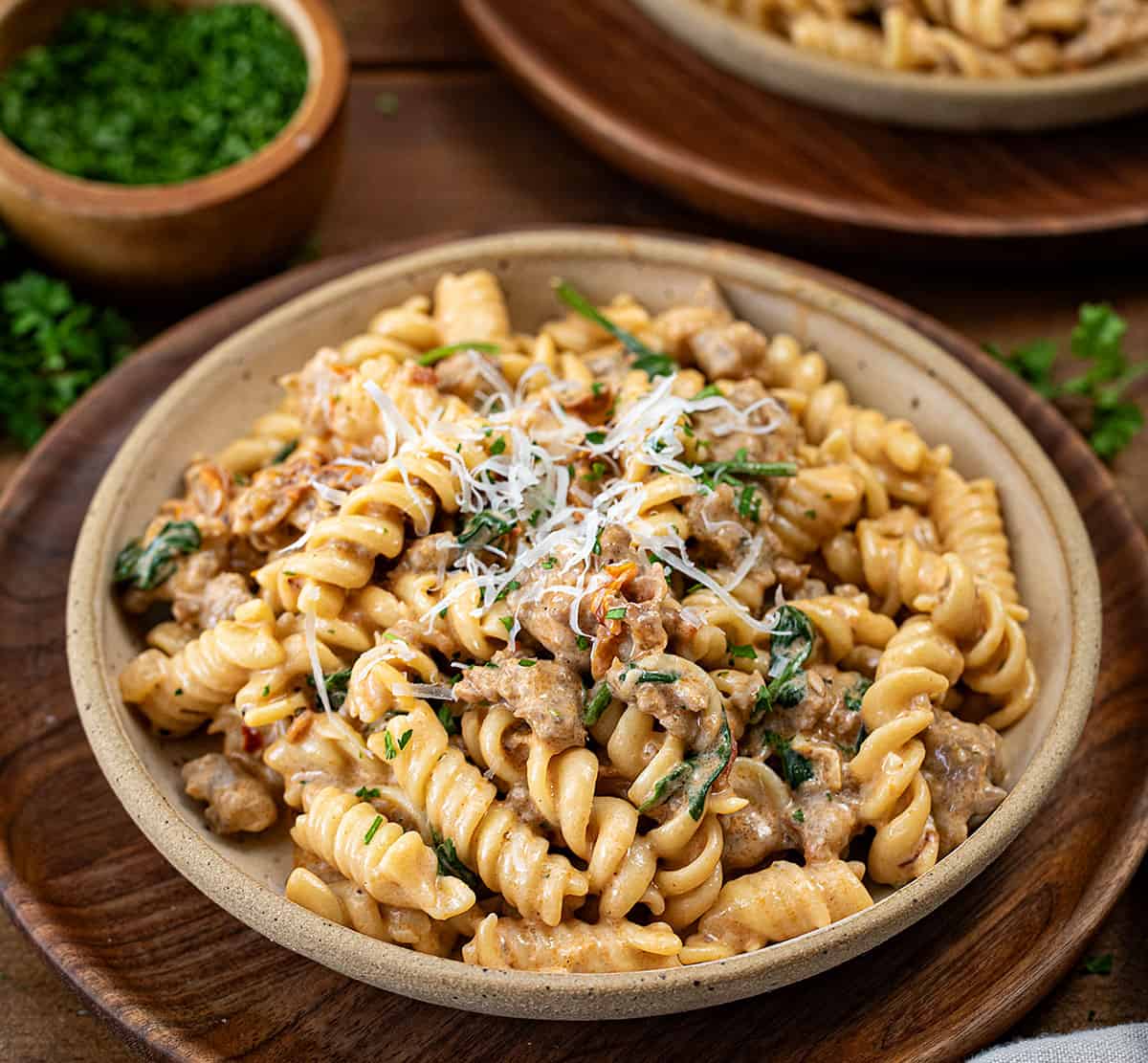 Plates of Creamy Italian Sausage Pasta on a wooden table.