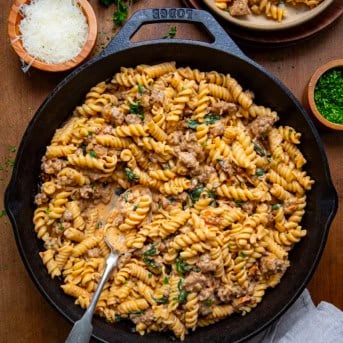 Skillet of Creamy Italian Sausage Pasta with a spoon on a wooden table from overhead.