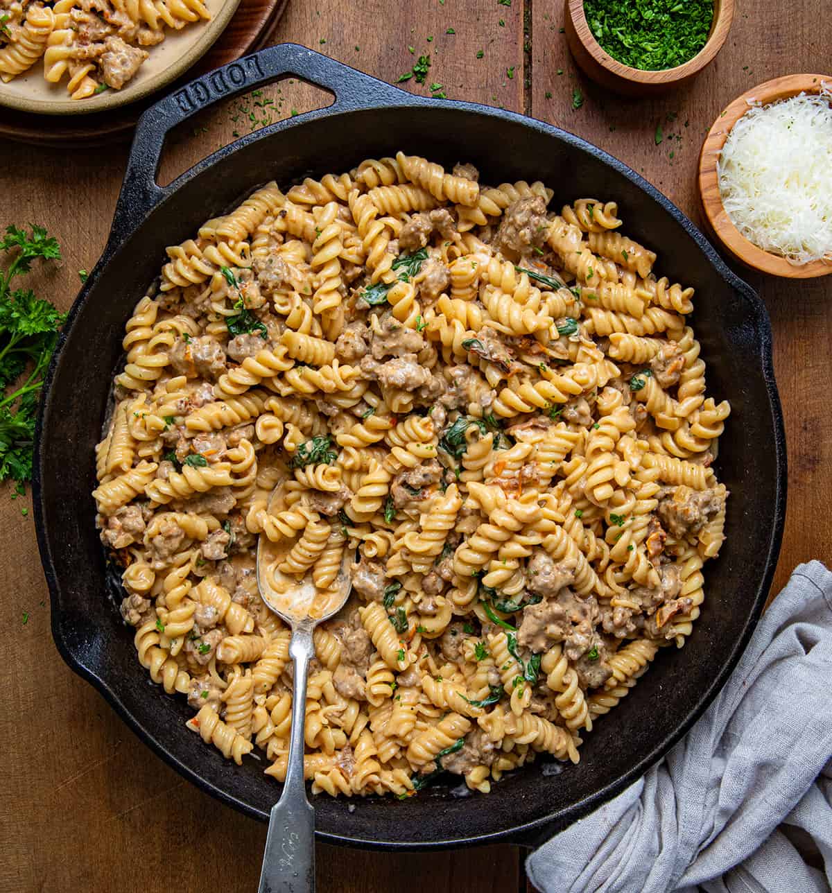 Skillet of Creamy Italian Sausage Pasta with a spoon on a wooden table from overhead.