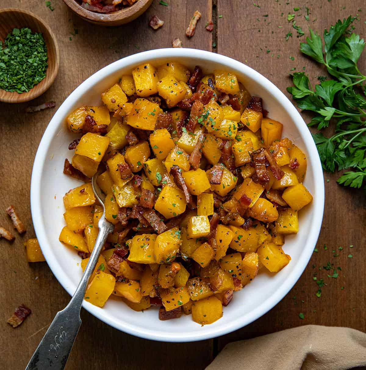 White bowl of Maple Bacon Butternut Squash on a wooden table from overhead.