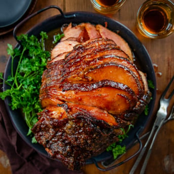 Whole Spiral Maple Bourbon Glazed Ham on a platter on a wooden table from overhead.