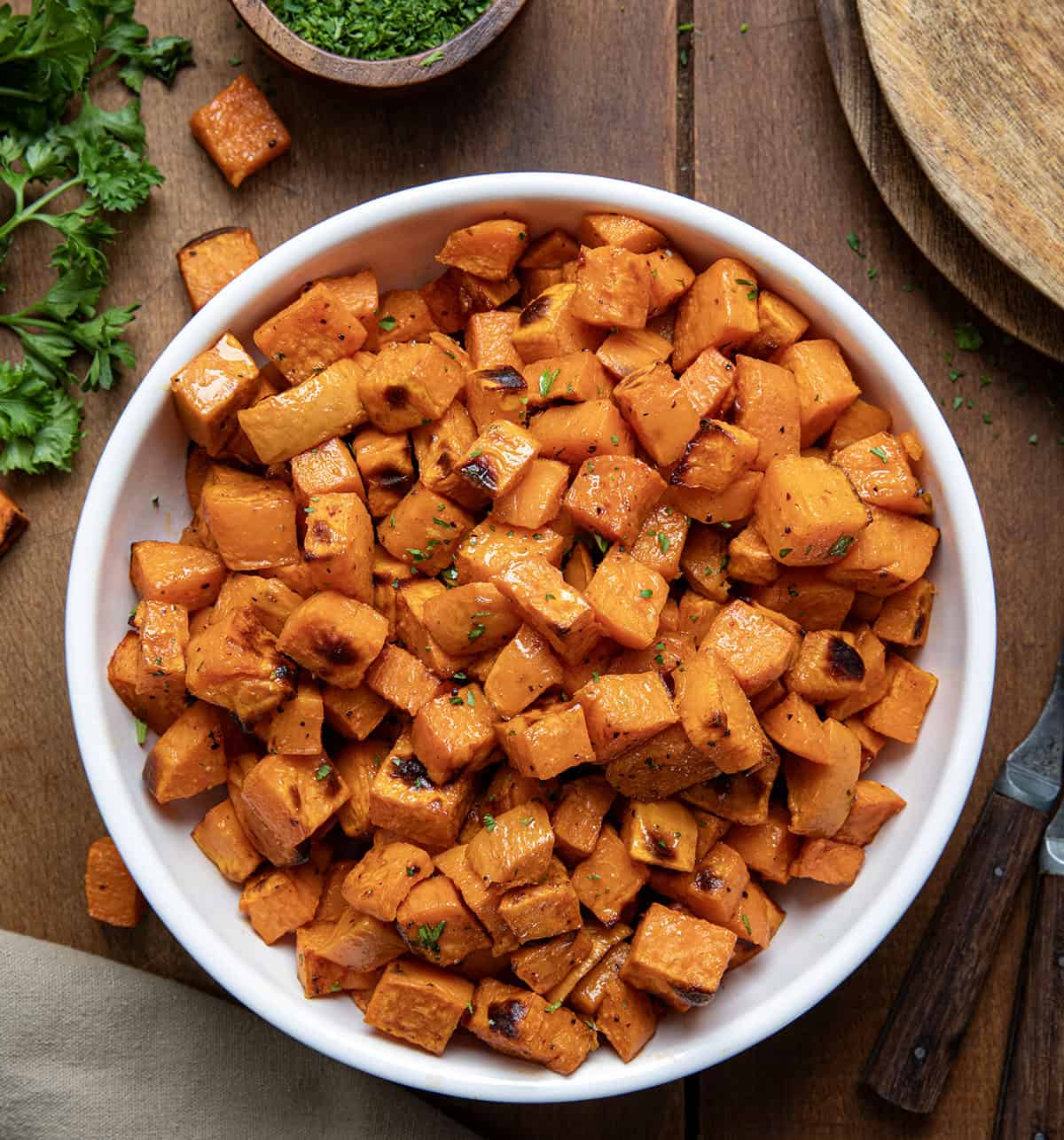 White serving bowl of Maple Chipotle Roasted Sweet Potatoes on a wooden table from overhead.