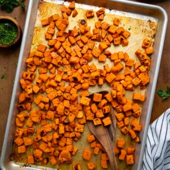 Sheet pan of Maple Chipotle Roasted Sweet Potatoes on a wooden table from overhead.