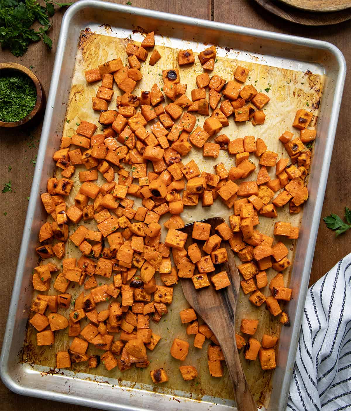 Sheet pan of Maple Chipotle Roasted Sweet Potatoes on a wooden table from overhead.