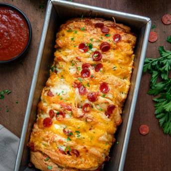 Loaf pan filled with Pepperoni Pull Apart Bread on a wooden table from overhead.