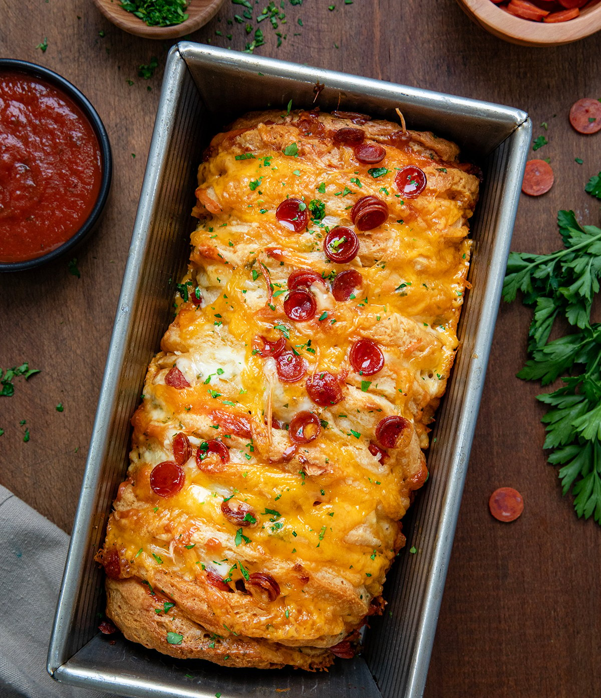 Loaf pan filled with Pepperoni Pull Apart Bread on a wooden table from overhead.