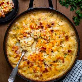 Skillet of Ranch Scalloped Potatoes and Ham on a wooden table with a spoon from overhead.