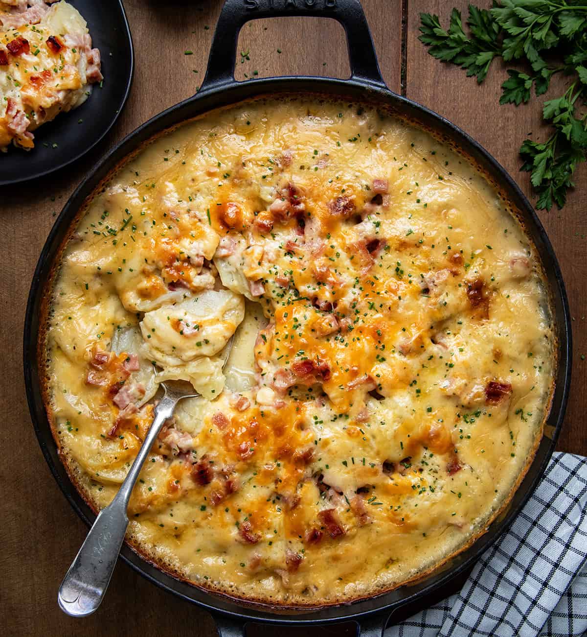 Skillet of Ranch Scalloped Potatoes and Ham on a wooden table with a spoon from overhead.